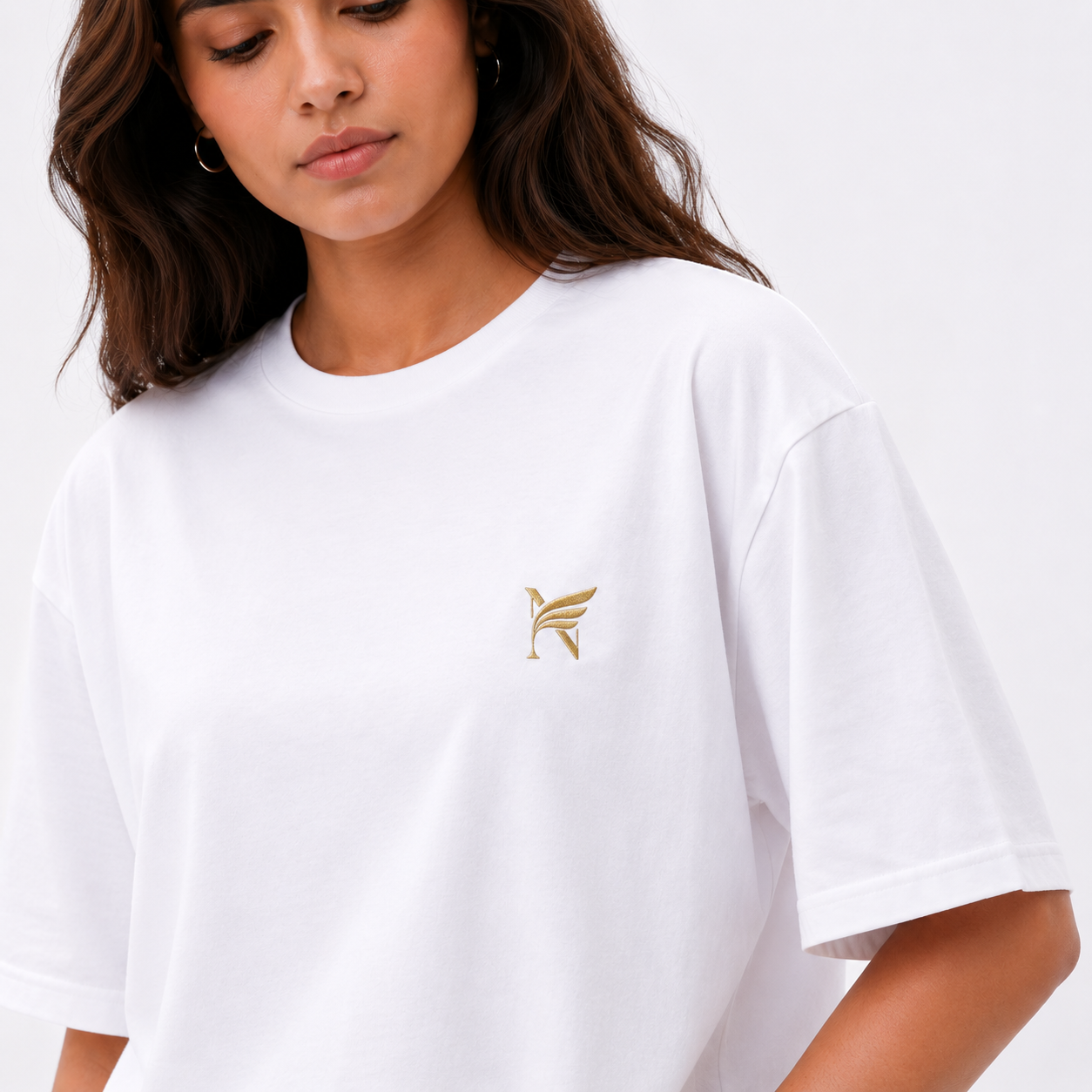 Person wearing a white t-shirt with a gold logo on a plain background